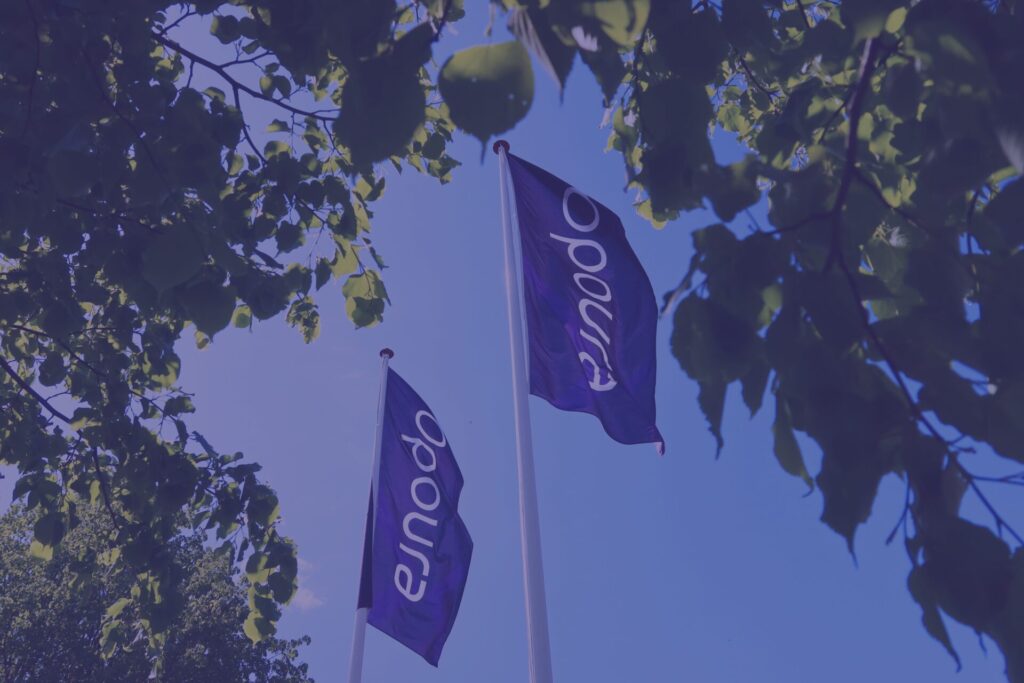 Opoura ESG report 2024 – Opoura flags waving in the blue sky among trees