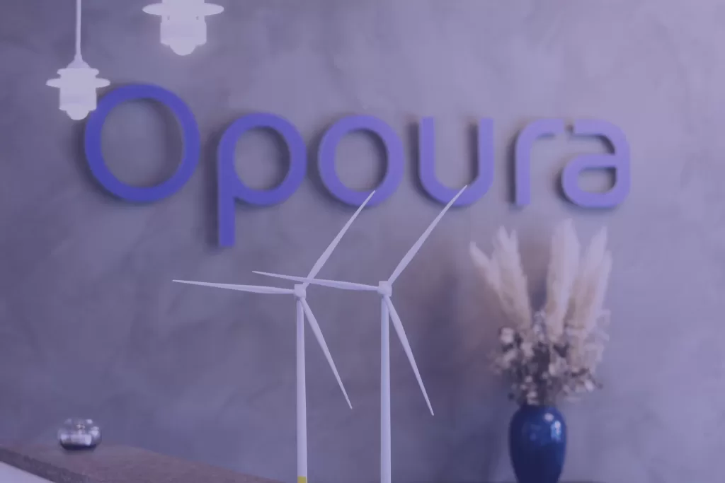Entrance to Opoura with company sign and wind turbines visible behind